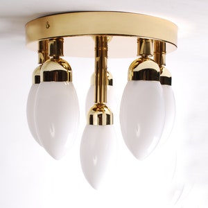 Könnte beinhalten: Eine goldene Deckenleuchte mit fünf weißen, mattierten Glasbirnen in Tropfenform.