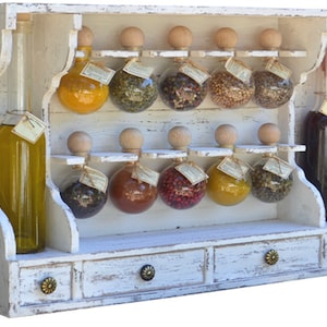 Peut inclure: Étagère à épices en bois blanc avec trois tiroirs et des bocaux en verre remplis de différentes épices. L'étagère a une finition blanche vieillie et présente des détails décoratifs.