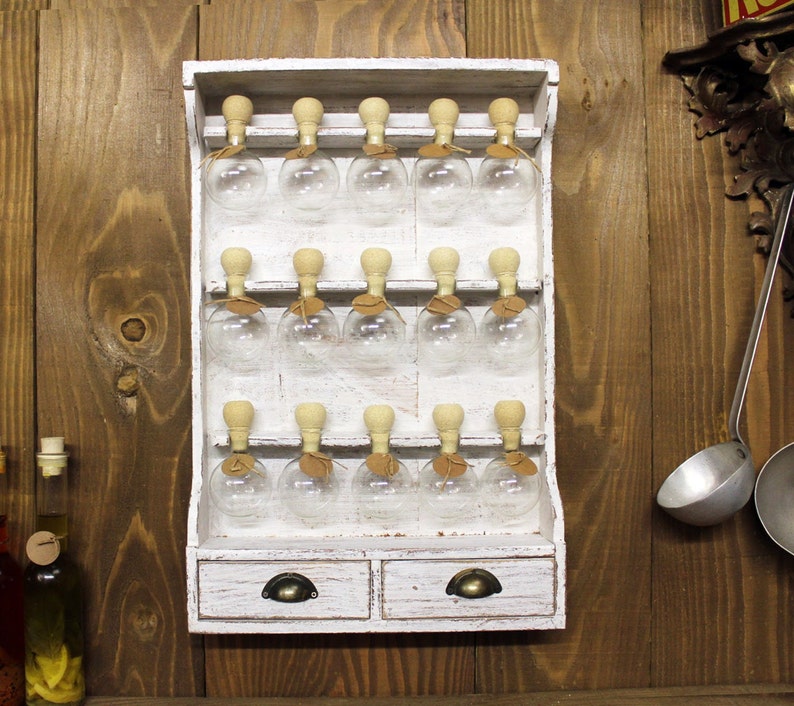 May include: White wooden spice rack with 18 glass jars with cork tops. The rack has two drawers with metal handles.