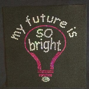 May include: A pink light bulb with the words "My future is so bright!" in white sequins on a black background.