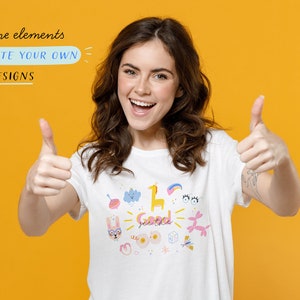 May include: A woman wearing a white t-shirt with a colorful graphic design featuring various illustrations, including a bunny, a cloud, a giraffe, a rainbow, and the words "See the good". She is giving a thumbs up with both hands and smiling. The background is a bright yellow.
