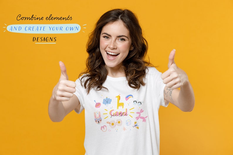 May include: A woman wearing a white t-shirt with a colorful graphic design featuring various illustrations, including a bunny, a cloud, a giraffe, a rainbow, and the words "See the good". She is giving a thumbs up with both hands and smiling. The background is a bright yellow.