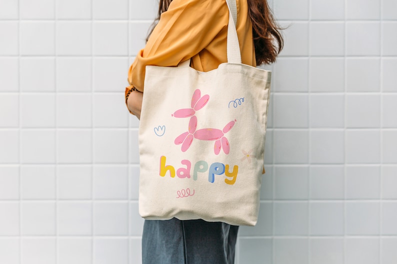 May include: A white canvas tote bag with a pink balloon animal design and the word "happy" in colorful letters.
