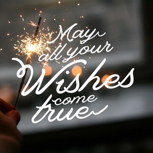 以下が含まれることがあります： 白い背景に、スパークラーと「May all your wishes come true」というテキストが書かれた画像です。