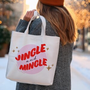 May include: A white tote bag with the words "Jingle and Mingle" in red script and a pink circle. Gold stars are scattered around the text. The bag is carried by a person wearing a gray coat and a brown hat.