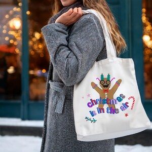 K&ouml;nnte beinhalten: Wei&szlig;e Stofftasche mit einem Lebkuchenmann-Motiv und dem Text "Christmas is in the air".