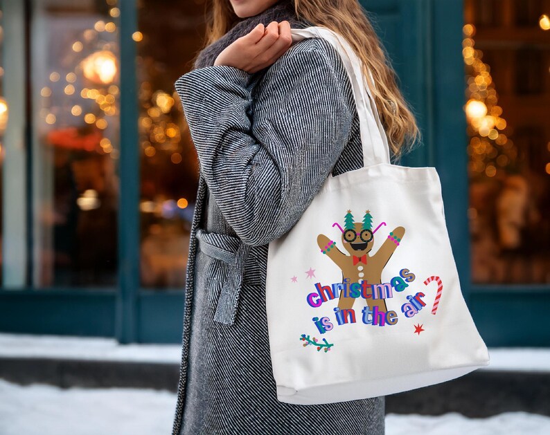 K&ouml;nnte beinhalten: Wei&szlig;e Stofftasche mit einem Lebkuchenmann-Motiv und dem Text "Christmas is in the air".