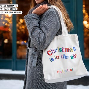 May include: A white tote bag with the text "Christmas is in the air" in colorful letters and "FaLaLa!" in red. The bag is carried by a person wearing a gray coat. The text "COMBINE ELEMENTS WITH EACH OTHER AND MAKE YOUR OWN PRINTS" is also visible.