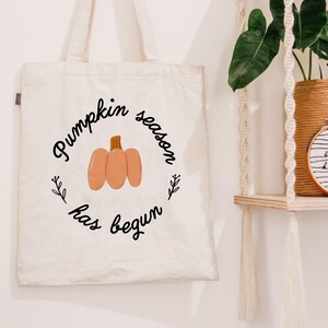 May include: A white canvas tote bag with the text "Pumpkin season has begun" in black lettering and a small orange pumpkin illustration.