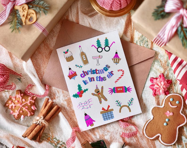 K&ouml;nnte beinhalten: Eine wei&szlig;e Karte mit bunten Illustrationen von weihnachtlichen Motiven, darunter ein Lebkuchenmann, Zuckerstangen und ein Weihnachtsbaum. Der Text "Christmas is in the air" ist in einer bunten Schrift geschrieben.