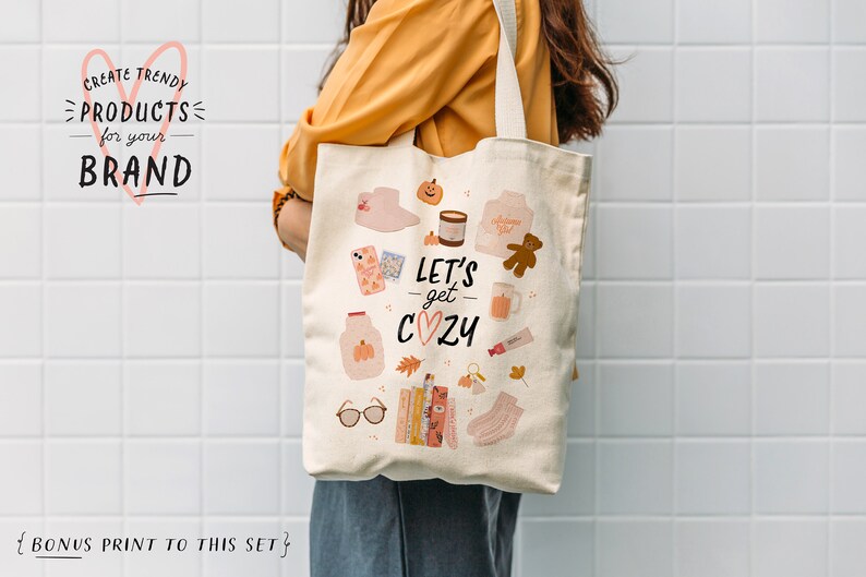 May include: A beige tote bag with a design featuring a variety of autumn-themed illustrations, including a pumpkin, a mug, a teddy bear, and the text "Let's get cozy".