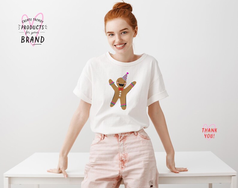 K&ouml;nnte beinhalten: Ein wei&szlig;es T-Shirt mit einem Lebkuchenmann, der einen Partyhut und eine Schleife tr&auml;gt. Der Lebkuchenmann ist braun mit wei&szlig;en Zuckergussdetails. Das T-Shirt wird von einer Frau in rosa Shorts getragen.