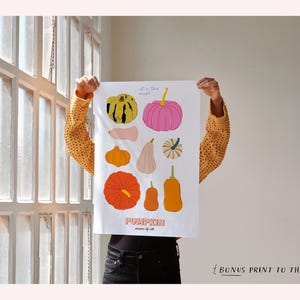 May include: A white print with colorful illustrations of different types of pumpkins. The print has the text "It's the most... Pumpkin" and "Season of all".