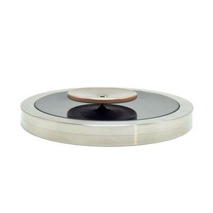 Puede incluir: Un tocadiscos redondo de color plateado con una plataforma circular negra y un pequeño disco marrón claro en la parte superior.