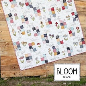 May include: A white quilt with a patchwork design featuring squares of various colors and patterns. The quilt includes embroidered flowers and words like "Bloom", "Love", and "Happy". The quilt measures 45 x 45 inches.