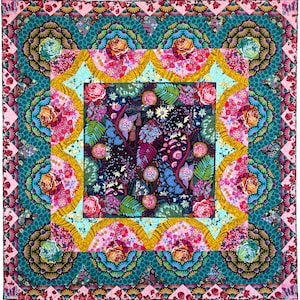 Puede incluir: Una colcha colorida con un cuadrado central que presenta un patrón floral rodeado por un borde de formas geométricas. La colcha está hecha de varias telas en tonos de rosa, azul, verde y amarillo.