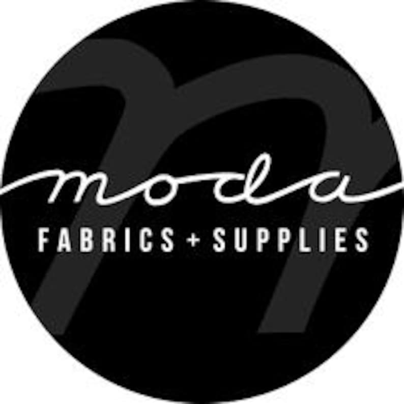 May include: A black and white circular logo for Moda Fabrics + Supplies. The word "moda" is written in a cursive font, with "FABRICS + SUPPLIES" in a sans-serif font below it.