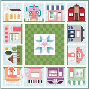 May include: A colorful quilt featuring various house and shop designs, including a church, a teapot, and a shop with a striped awning. The quilt has a central star pattern with the words "Our Season" and is bordered by a light blue floral pattern.