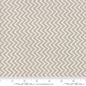 Può includere: Un primo piano di un tessuto beige con un motivo a chevron bianco. Il tessuto è misurato con un righello che indica "moda" ai segni di 5 cm e 15 cm.