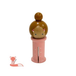 May include: A wooden doll with brown hair and a pink dress with white polka dots. The doll is holding a needle and thread.