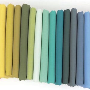 May include: A collection of folded fabric in a spectrum of colors, ranging from light peach and coral to mustard yellow and olive green, transitioning to teal, gray, and ending with shades of pink and beige. The fabric appears to be soft and smooth.