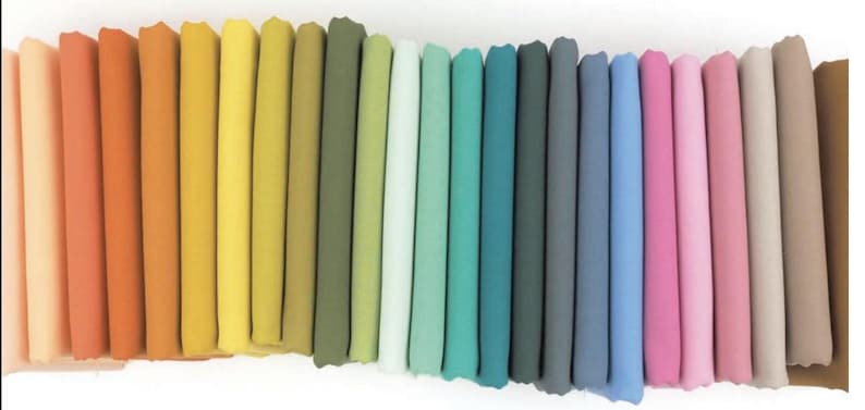 May include: A collection of folded fabric in a spectrum of colors, ranging from light peach and coral to mustard yellow and olive green, transitioning to teal, gray, and ending with shades of pink and beige. The fabric appears to be soft and smooth.