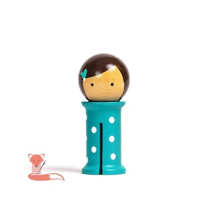 May include: A wooden doll with a brown hair and a teal bow, atop a teal spool with white polka dots. The doll's face is painted with a light skin tone, black eyes, and a small smile. The spool has a vertical slit.