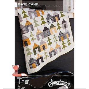 May include: A quilt pattern called "Base Camp" featuring a white background with a repeating pattern of small houses and trees in shades of green, black, gray, and yellow. The quilt is 60 inches by 55 inches and is made with fabric from the "Timisr" collection by Sweetwater.