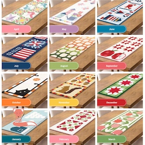 May include: A collection of twelve rectangular table runners, each with a unique design representing a month of the year. Designs include geometric patterns, seasonal motifs like apples, squirrels, and foxes, and text labels for each month.