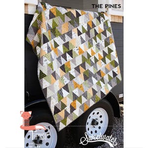 May include: A patchwork quilt with a geometric triangle pattern in shades of green, gray, white, and orange. The quilt is labeled "The Pines" and measures 60 x 64 inches. The Sweetwater logo is visible.