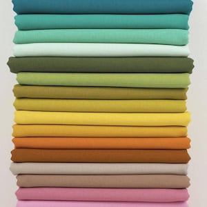 May include: A stack of folded fabric in a variety of colors, ranging from blues and greens to yellows, oranges, and pinks. The fabric appears to be cotton or a similar material, with a smooth, even texture. The colors are vibrant and well-saturated.