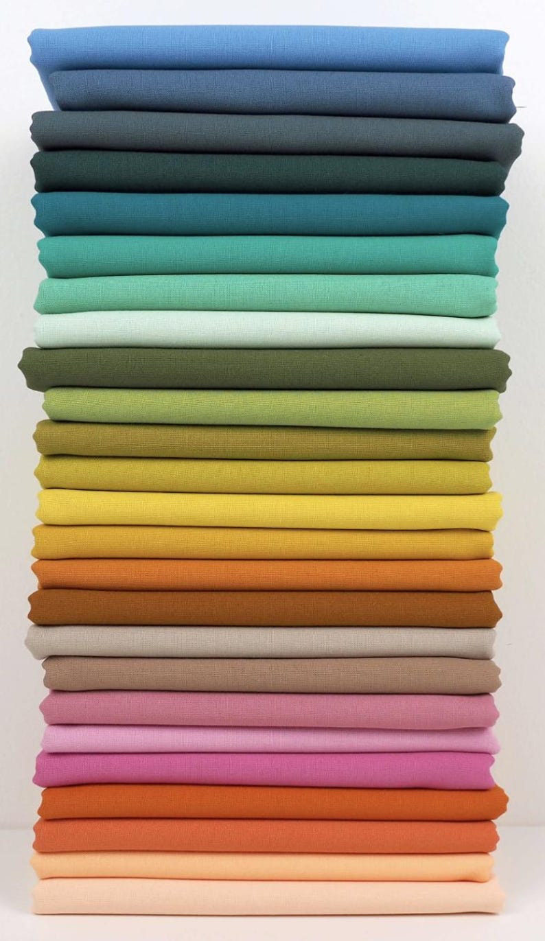 May include: A stack of folded fabric in a variety of colors, ranging from blues and greens to yellows, oranges, and pinks. The fabric appears to be cotton or a similar material, with a smooth, even texture. The colors are vibrant and well-saturated.