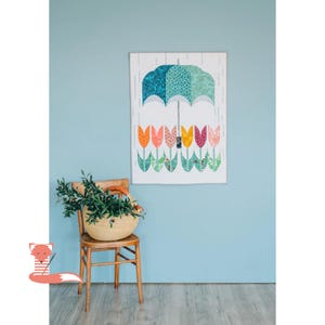 Könnte beinhalten: Ein farbenfrohes Wandbild mit einem Schirm-Design mit einem türkis-grünen Baldachin und einer Reihe von Tulpen in Orange, Rosa, Gelb und Grün. Ein geflochtener Korb mit Grünzeug steht auf einem Holzstuhl.