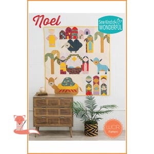 May include: A quilt with a nativity scene design, featuring figures, animals, and buildings in various colors. The word "Noel" is written in red at the top left. The quilt hangs above a wooden dresser with three drawers.