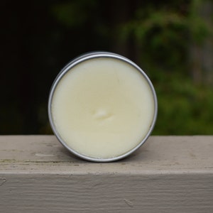 May include: A round tin container with a white, creamy substance inside. The tin is silver and has a smooth surface.