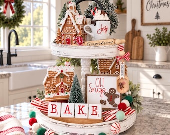 Può includere: Un vassoio a due livelli in legno bianco anticato decorato con ornamenti a forma di casetta di pan di zenzero, una tazza con la scritta Joy, un cartello con Oh Snap e un omino di pan di zenzero, e tessere che compongono la parola BAKE.