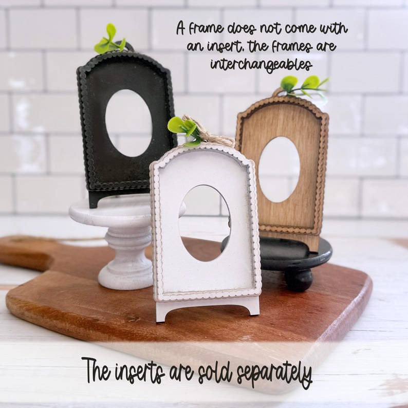 May include: Three arched picture frames in black, white, and natural wood, each featuring a scalloped edge and a central oval cutout. Each frame is topped with a small green leaf accent. Text reads: A frame does not come with an insert. The frames are interchangeable. The inserts are sold separately.