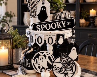 May include: A two-tiered white wooden tray decorated for Halloween with black and white items including a SPOOKY St sign, a BOO banner, ghost-shaped tags, a round sign with a spider web and the word eek, and a small white pumpkin.