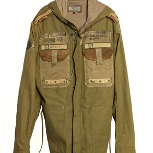 May include: A green hooded jacket with multiple pockets and patches. The patches include "US" and "MASK CHEMICAL-BIOLOGICAL FIELD. M17A2".