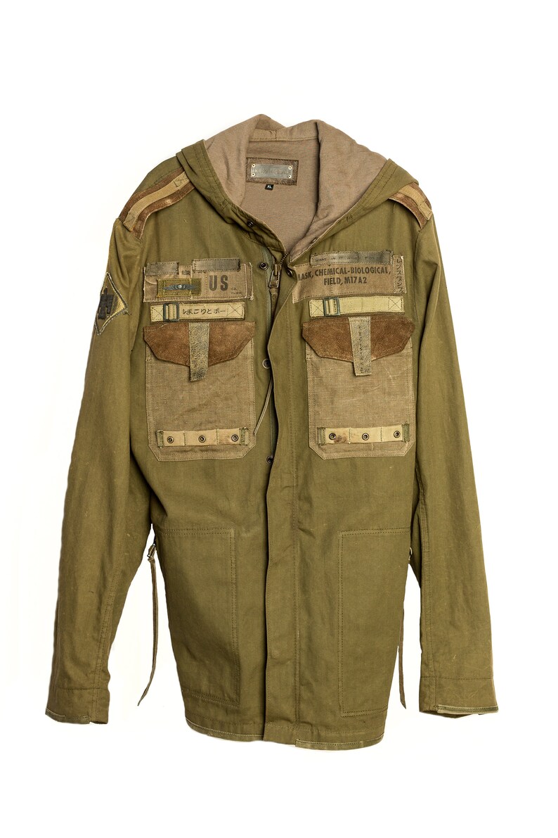 May include: A green hooded jacket with multiple pockets and patches. The patches include "US" and "MASK CHEMICAL-BIOLOGICAL FIELD. M17A2".