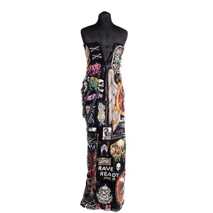 May include: A black strapless dress covered in colorful patches and embellishments. The patches feature various designs, including skulls, wings, and text. The dress is on a mannequin.