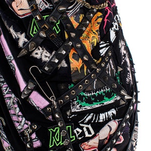 May include: A black leather jacket with multiple straps, studs, and safety pins. The jacket is decorated with patches, including a green and black patch with the word "Maled" in green letters.