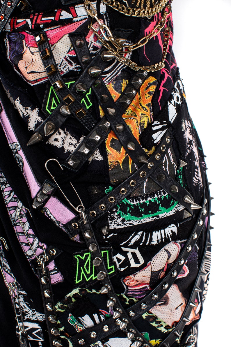 May include: A black leather jacket with multiple straps, studs, and safety pins. The jacket is decorated with patches, including a green and black patch with the word "Maled" in green letters.