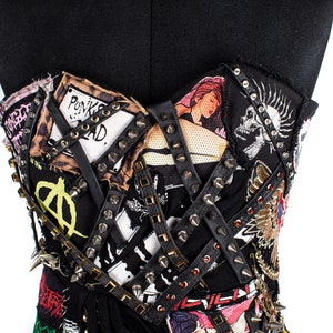 May include: A black strapless top with a punk rock aesthetic. The top is covered in patches, studs, and leather straps. Some of the patches include images of a skull, a woman, and the words "Punk's Not Dead."