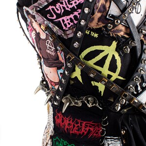 May include: A black corset with various punk rock band patches, including "Jungle Rot", "Anarchy", and "Le Temps", adorned with silver studs and black leather straps.