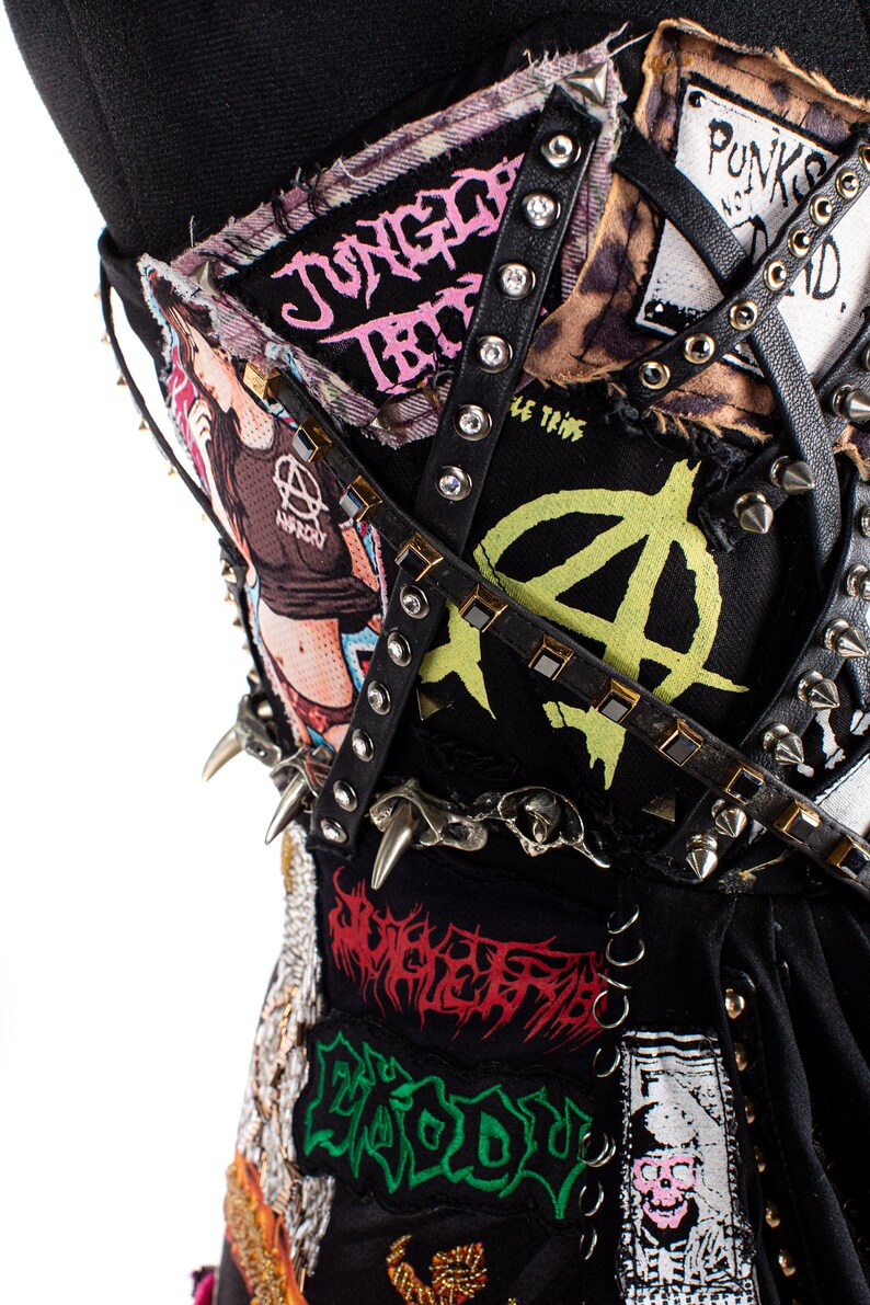 May include: A black corset with various punk rock band patches, including "Jungle Rot", "Anarchy", and "Le Temps", adorned with silver studs and black leather straps.