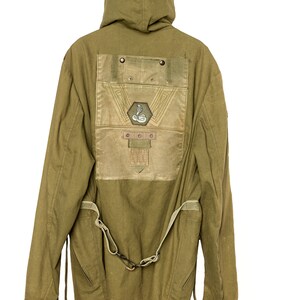 May include: A green hooded jacket with a large patch on the back. The patch features a snake design and a geometric pattern. The jacket has a belt and two pockets on the sides.