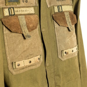 May include: A green utility shirt with multiple pockets and patches. The shirt has a large patch with a Native American design on the left side of the chest. The right side of the chest has a patch with the text "FIELD, WHITE" and a smaller patch with the text "US" and a graphic of a plane. The shirt also has a patch with Japanese text that reads "いんでこのコーナー".