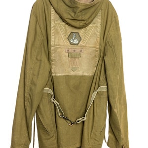 May include: A green hooded jacket with a brown patch on the back featuring a snake design and the text "DOOO". The jacket has a strap and buckle detail on the front.
