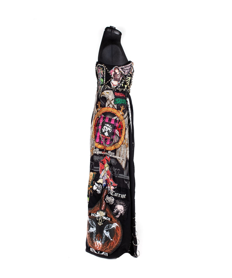 May include: A black maxi dress with a variety of colorful patches and embellishments. The patches feature images of skulls, eagles, and other graphic designs. The dress has a fitted bodice and a flowing skirt.